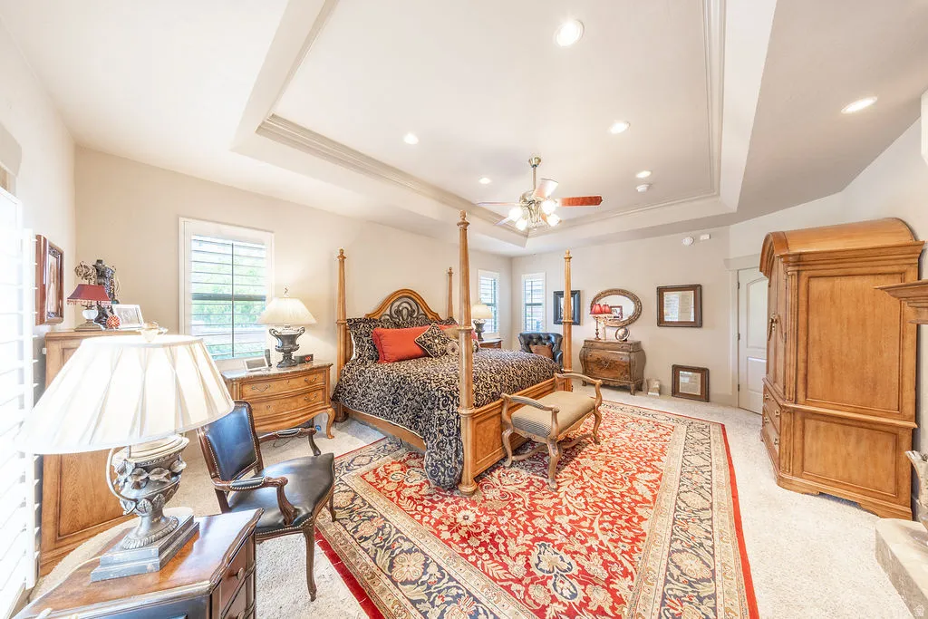 Bedroom featuring a raised ceiling, multiple windows, a ceiling fan, light carpet, and recessed lighting