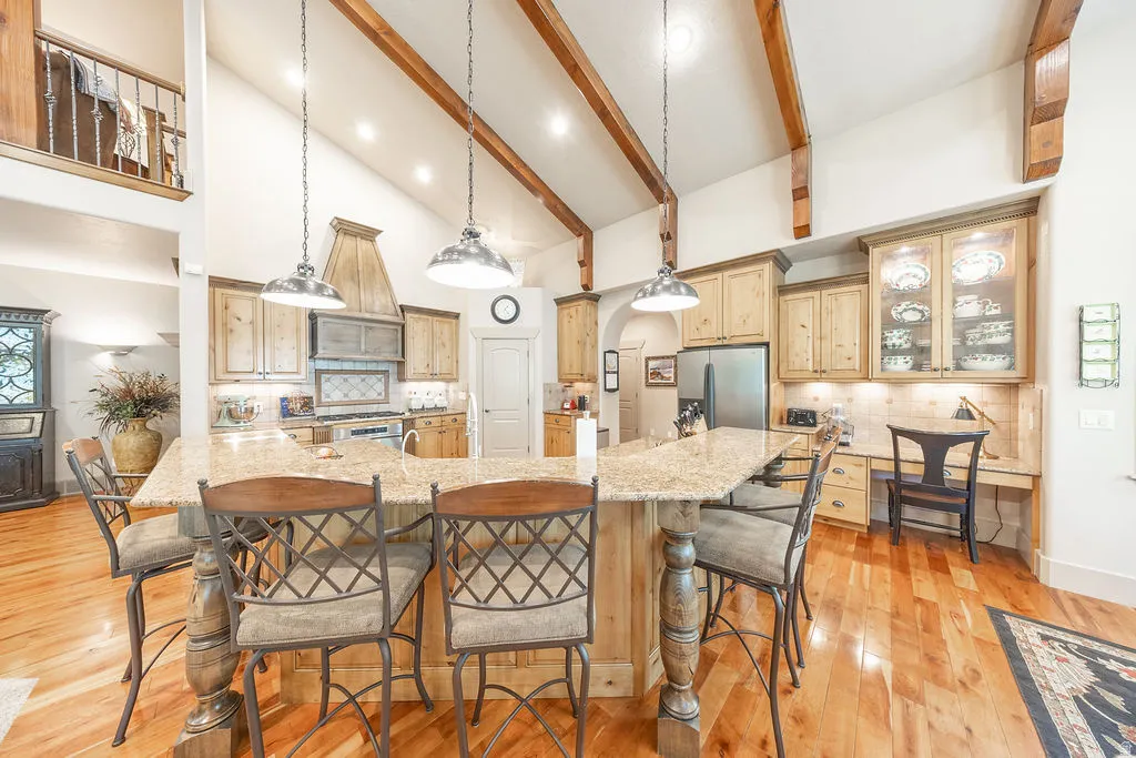 Kitchen with backsplash, a kitchen bar, light stone counters, light wood finish cabinets, and lofted ceiling