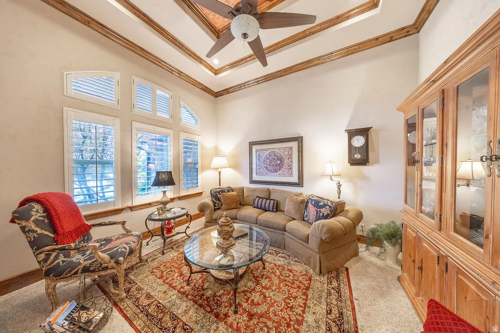 Living room featuring ceiling fan, light colored carpet, ornamental molding, and a high tray ceiling