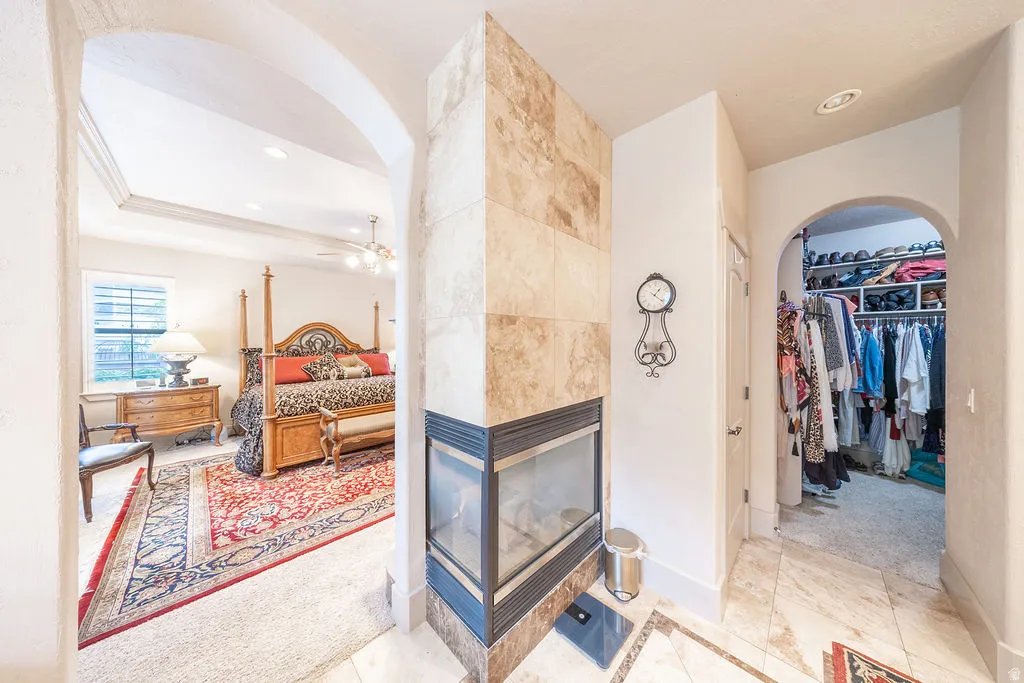Bedroom featuring arched walkways, a tiled fireplace, a walk in closet, light colored carpet, and recessed lighting