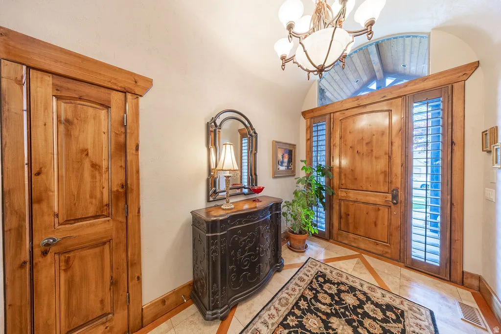 Entrance foyer featuring lofted ceiling, suspended lighting, inlaid floor details, and light tile patterned flooring