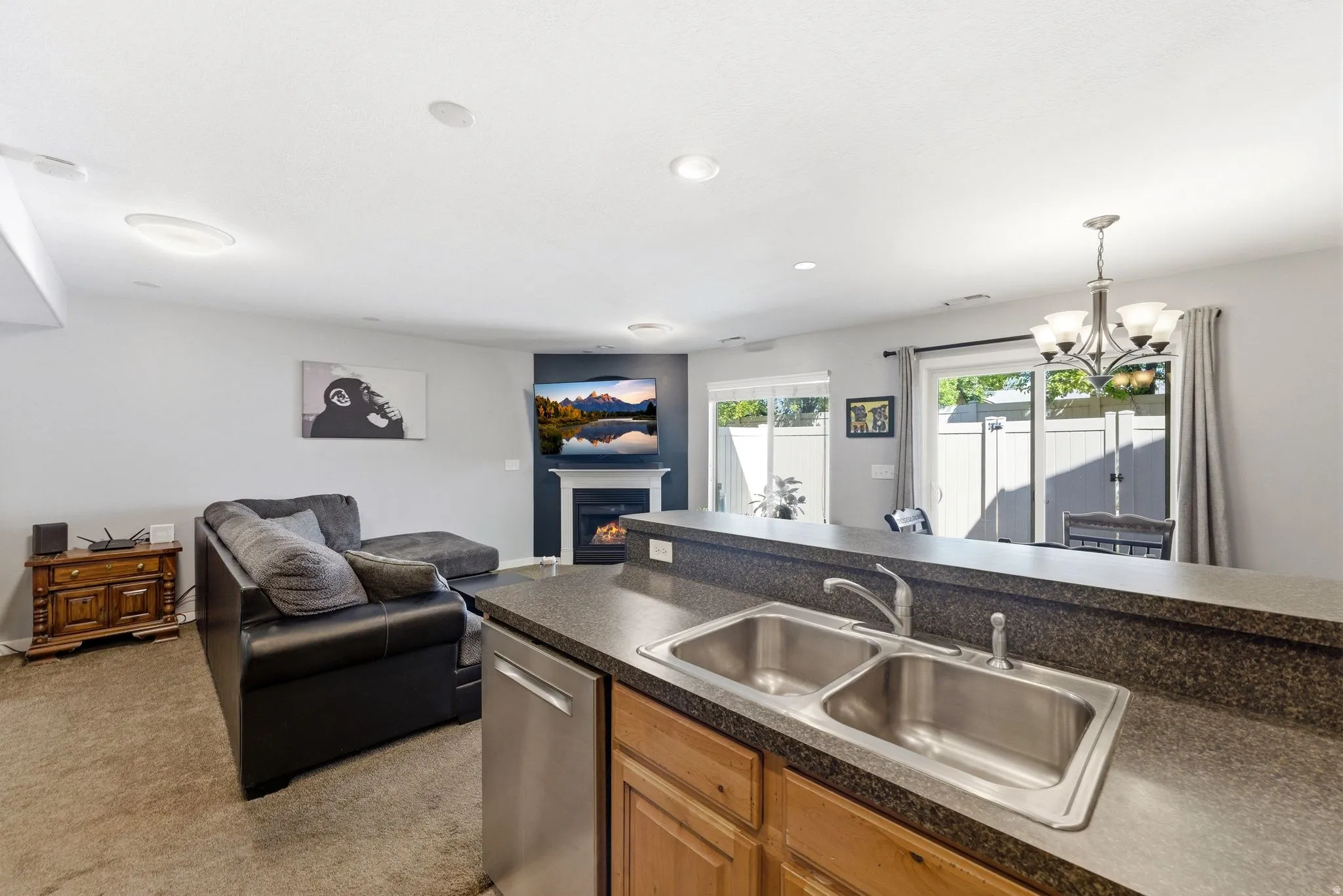 Kitchen featuring dark countertops, open floor plan, a lit fireplace, stainless steel dishwasher, and wood finish cabinets