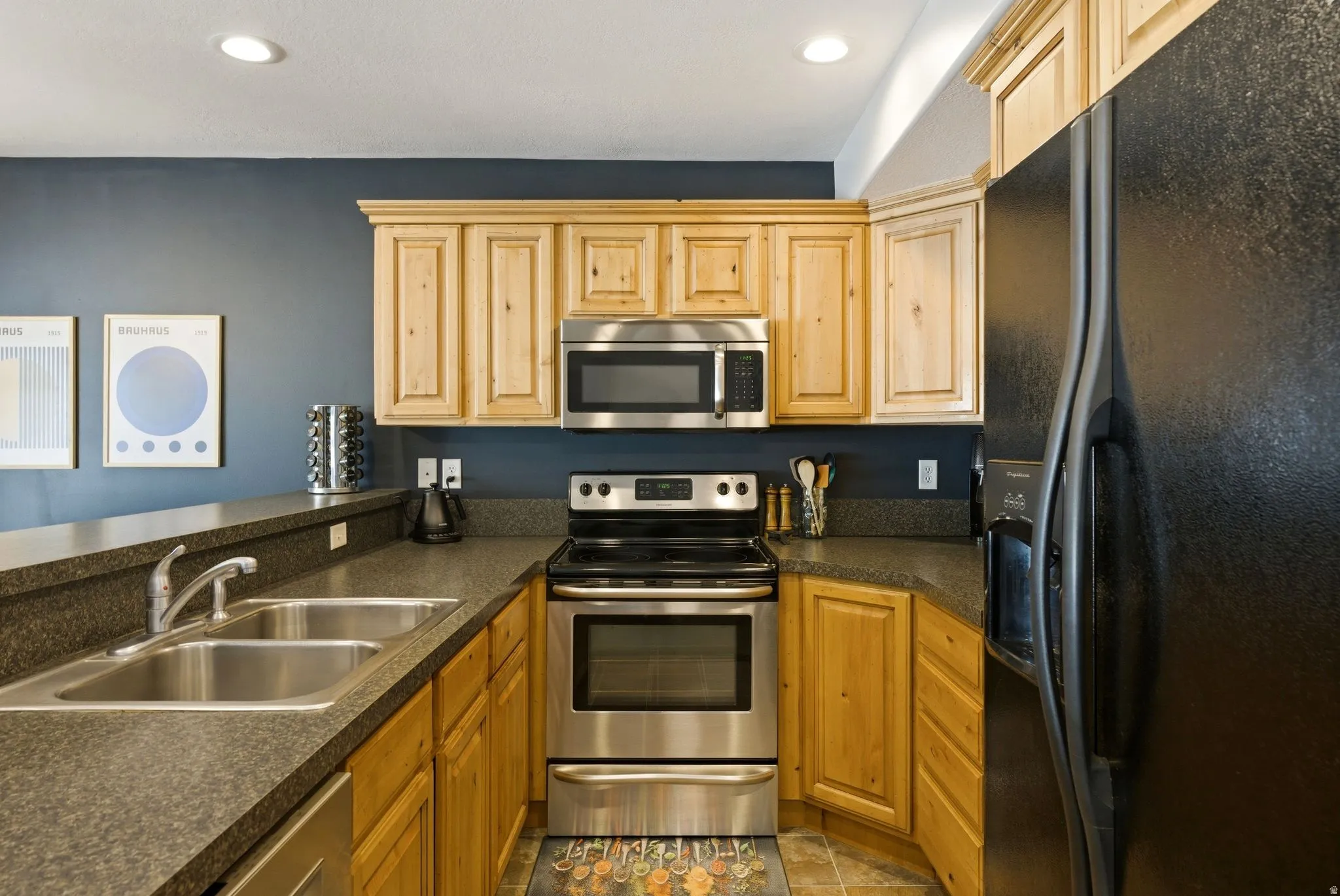 Kitchen with stainless steel appliances, dark countertops, recessed lighting, and light wood finish cabinets
