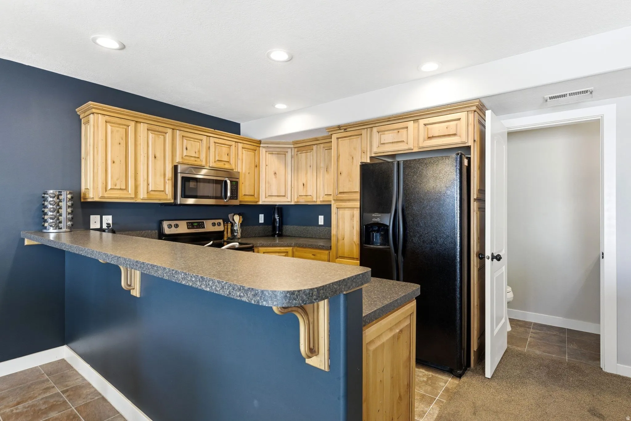 Kitchen featuring a breakfast bar, dark countertops, a peninsula, stainless steel appliances, and light wood finish cabinetry