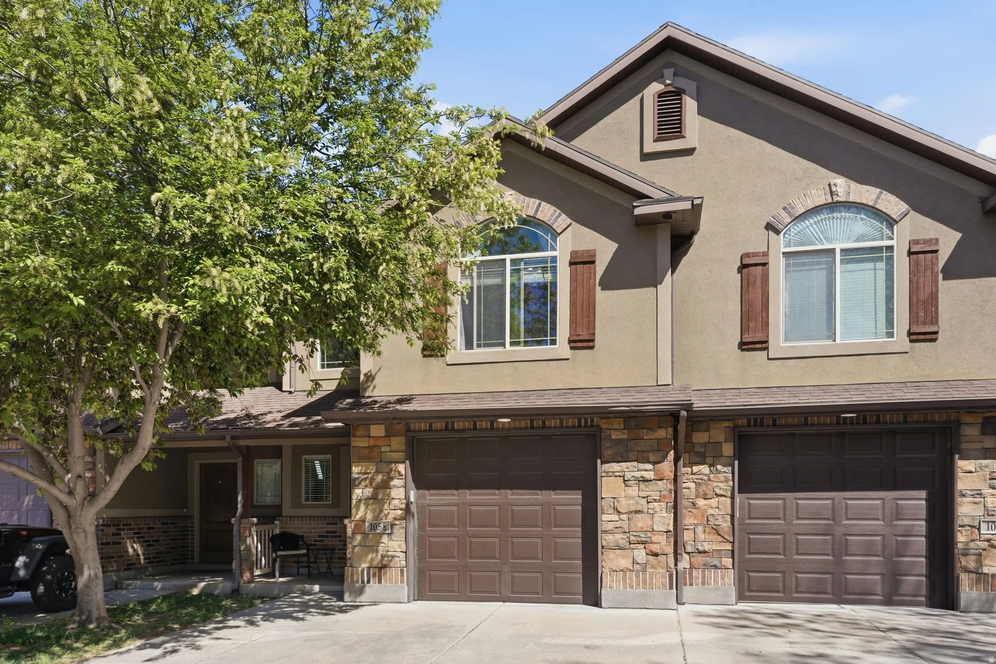 View of front of home featuring an attached garage, stucco siding, driveway, and stone siding