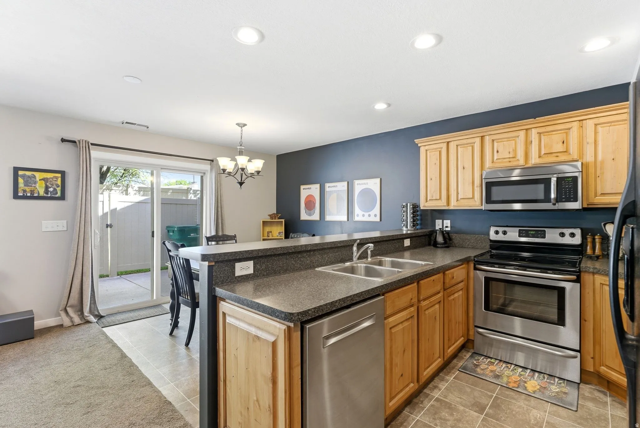 Kitchen featuring a peninsula, stainless steel appliances, dark countertops, hanging lights, and light tile patterned floors