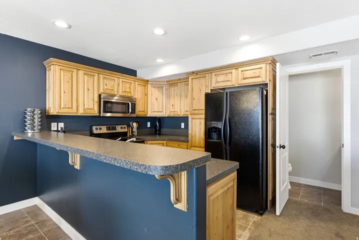 Kitchen featuring a breakfast bar, dark countertops, a peninsula, stainless steel appliances, and light wood finish cabinetry