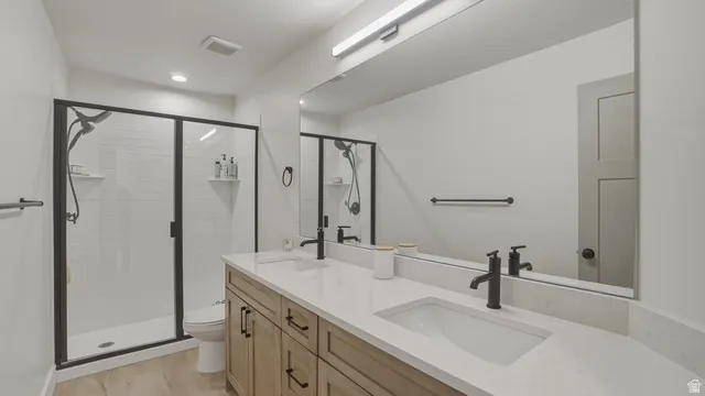 Full bath with double vanity, a stall shower, and light wood-style flooring