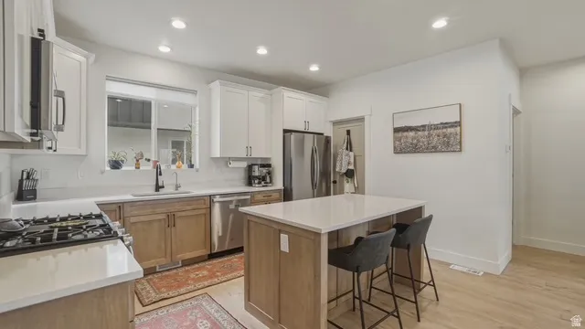Kitchen with a kitchen island, light wood-style flooring, stainless steel appliances, recessed lighting, and a breakfast bar