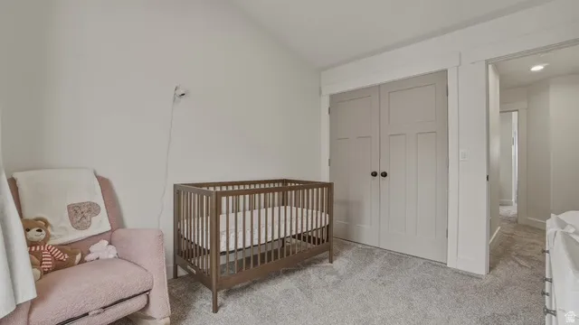 Bedroom with a crib, light colored carpet, a closet, and lofted ceiling