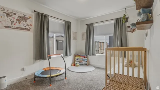 Bedroom with light colored carpet, a nursery area, and multiple windows