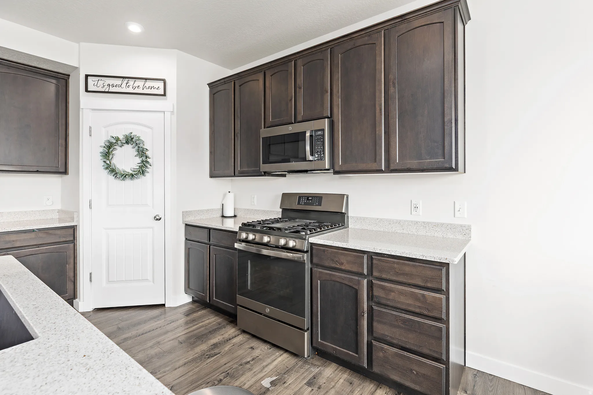 Kitchen with dark wood finish cabinets, stainless steel appliances, light stone counters, and dark wood-style flooring