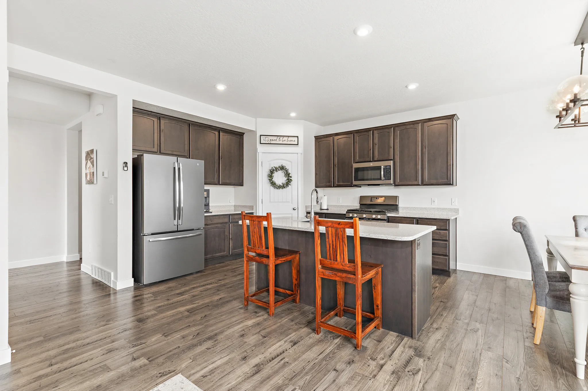 Kitchen featuring stainless steel appliances, a kitchen island with sink, dark wood finish cabinetry, dark wood-style flooring, and light stone counters