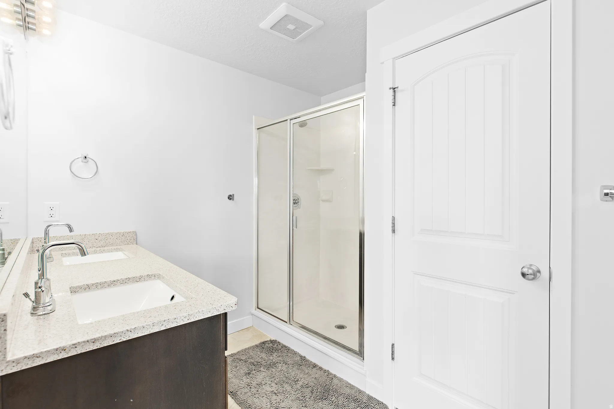 Full bath with double vanity, a shower stall, and a textured ceiling