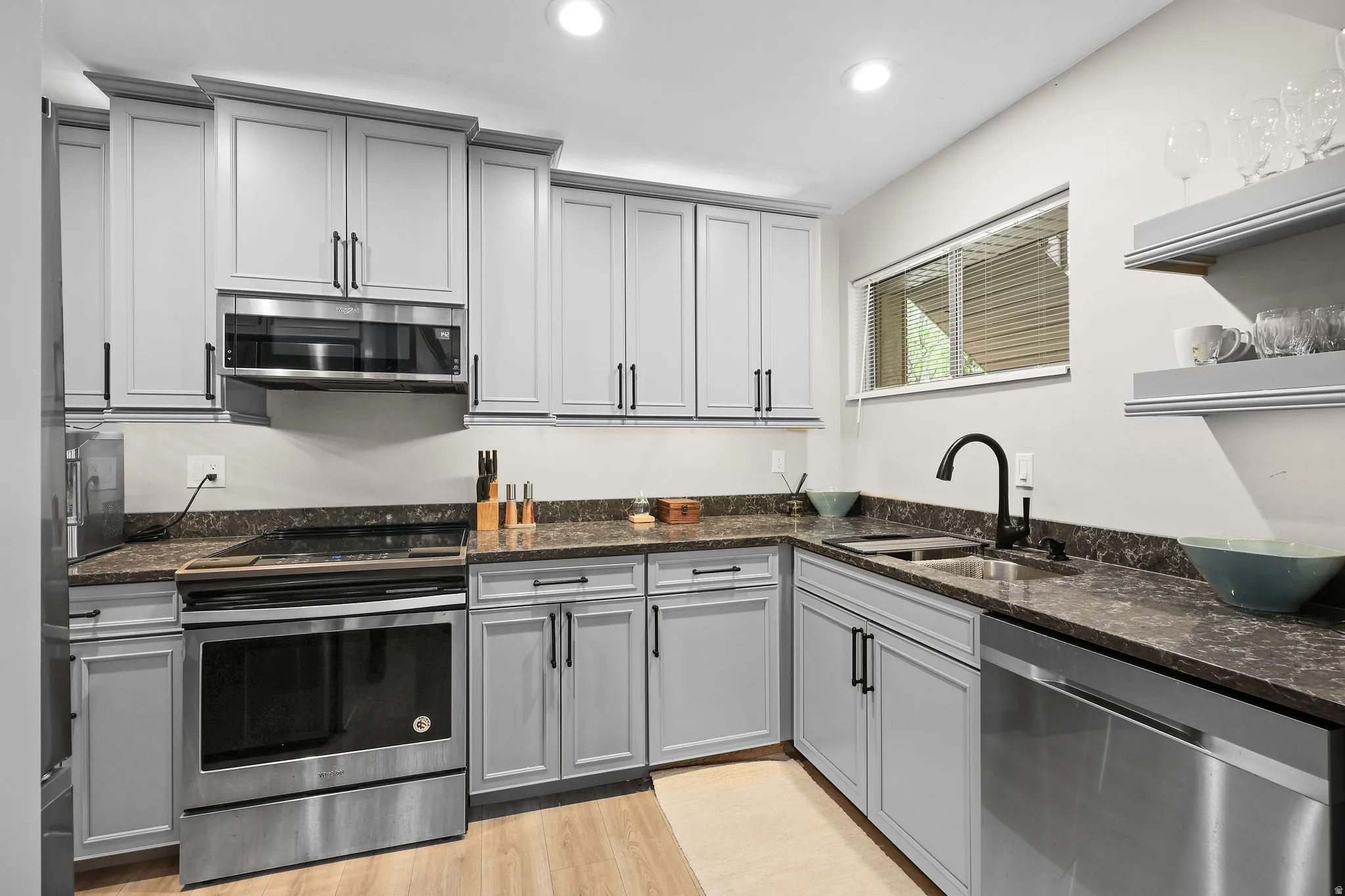 Kitchen with stainless steel appliances, dark stone countertops, gray cabinets, light wood-style floors, and recessed lighting