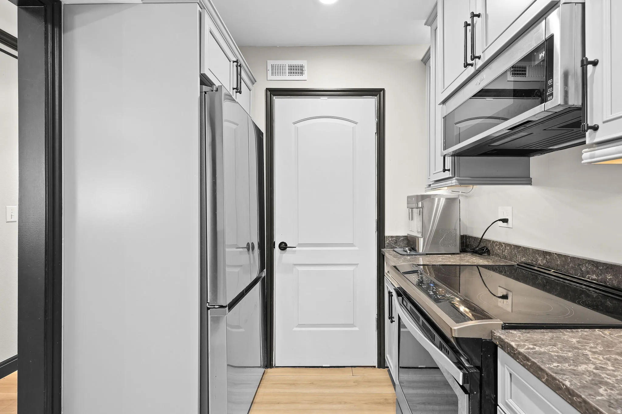 Kitchen with stainless steel appliances, light wood-type flooring, dark stone countertops, and recessed lighting