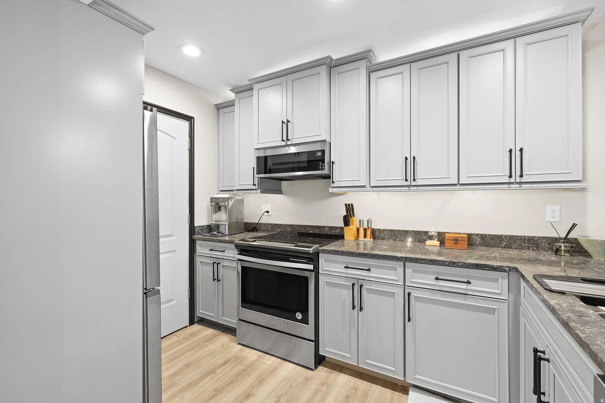Kitchen featuring stainless steel appliances, light wood-type flooring, gray cabinetry, dark stone counters, and recessed lighting