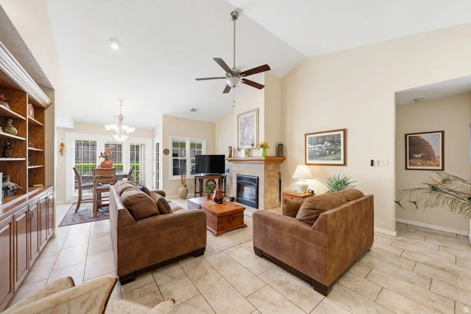 Living room with ceiling fan, a glass covered fireplace, lofted ceiling, suspended lighting, and light tile patterned floors