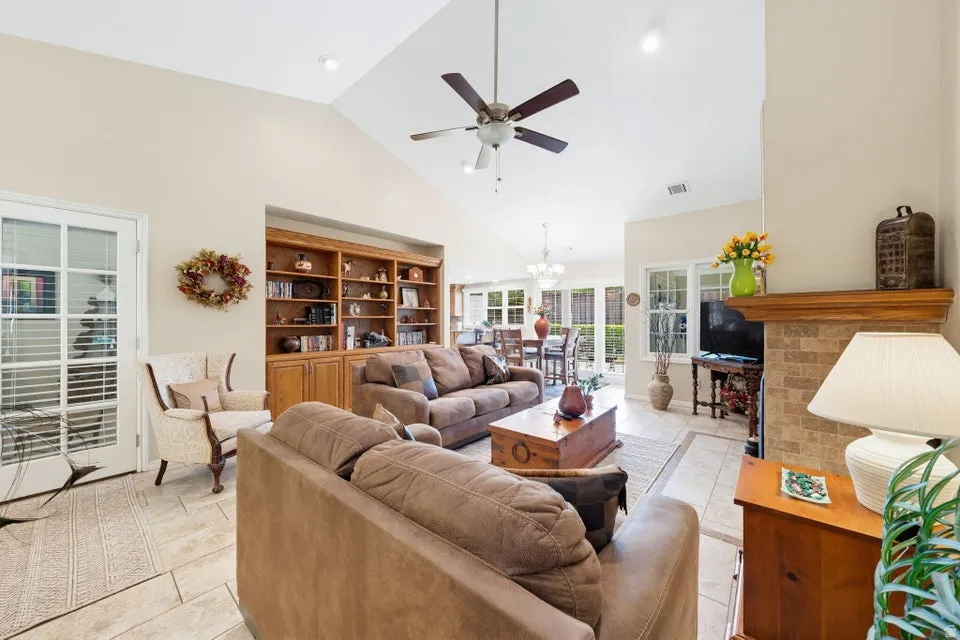 Living room featuring a ceiling fan, vaulted ceiling, light tile patterned floors, suspended lighting, and a fireplace