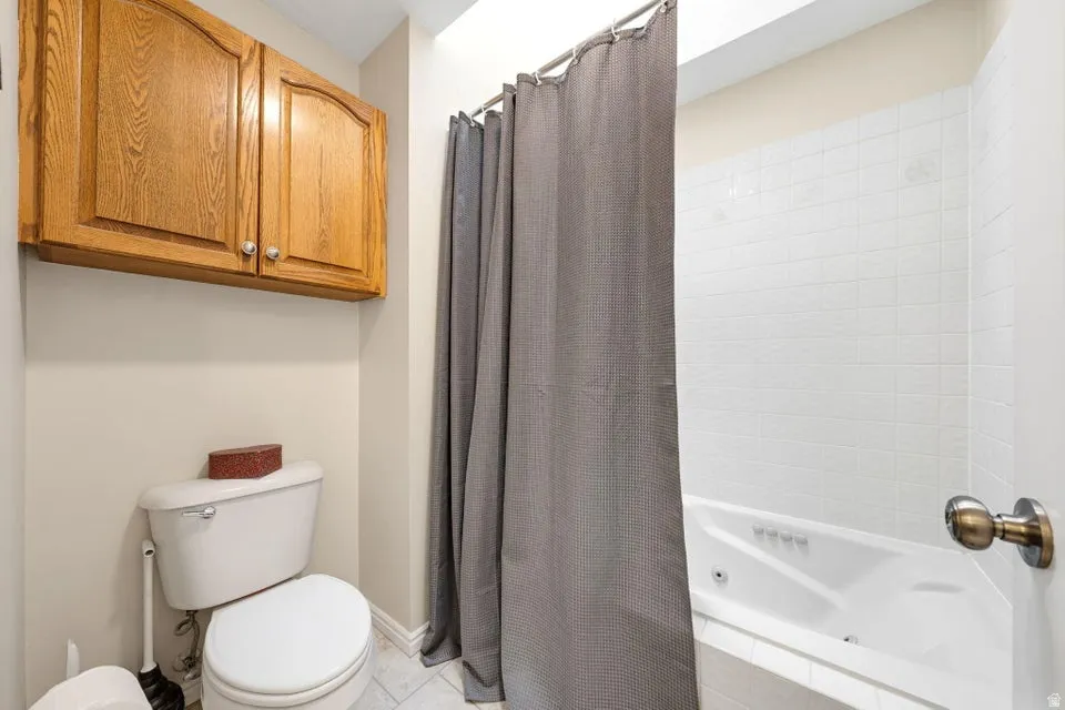 Full bathroom featuring toilet and a combined bath / shower with jetted tub