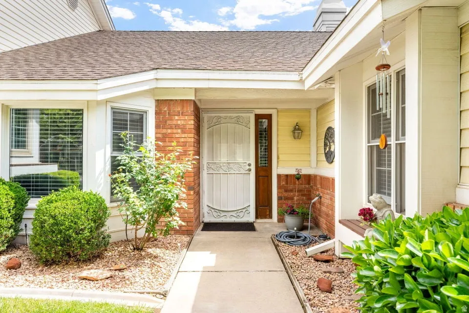 Entrance to property with brick siding, a shingled roof, a porch, and a chimney
