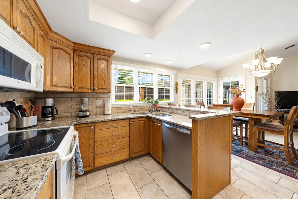 Kitchen featuring white appliances, wood finish cabinets, light stone countertops, hanging lights, and lofted ceiling