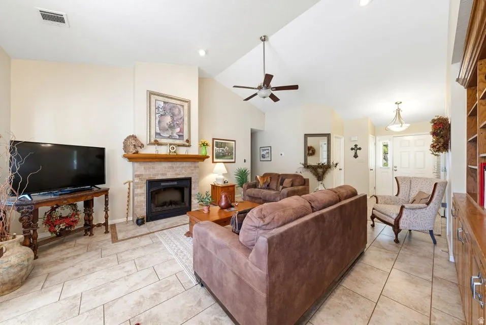 Living room with a fireplace with raised hearth, lofted ceiling, a ceiling fan, and light tile patterned floors