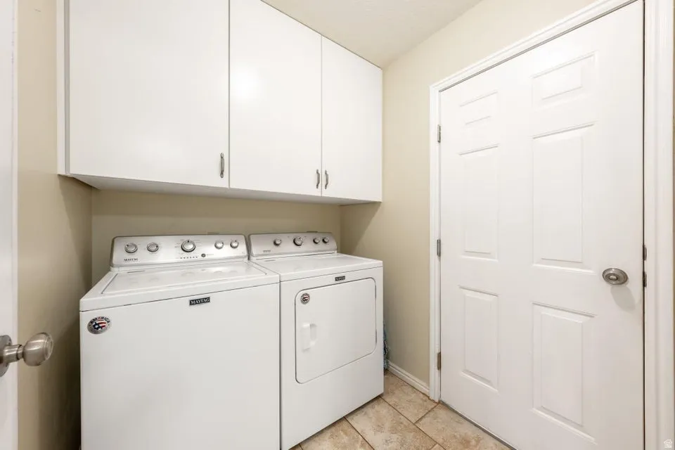 Laundry room featuring washing machine and dryer, cabinet space, and light tile patterned flooring