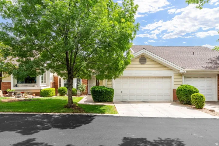 View of property hidden behind natural elements with brick siding, roof with shingles, concrete driveway, and an attached garage