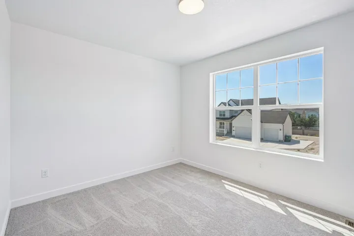 Bright room featuring a large multi-pane window, flush-mount ceiling light, light gray carpet, white baseboards, and white walls