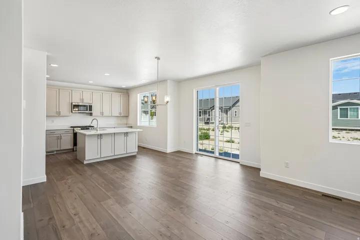 Open-concept living area with wood-finish flooring, a kitchen island, contemporary pendant lighting, recessed ceiling lights, and sliding glass doors