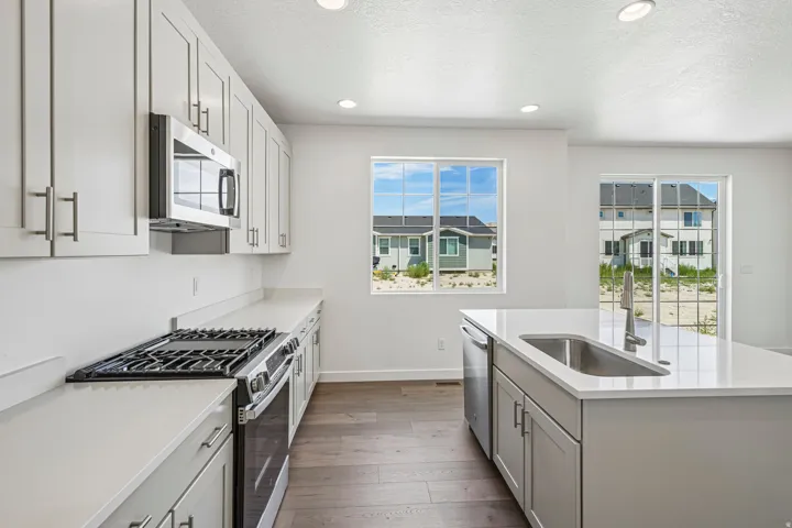 Contemporary kitchen featuring white cabinetry, light-toned countertops, stainless steel appliances, a center island with an undermount sink, and wood-finish flooring