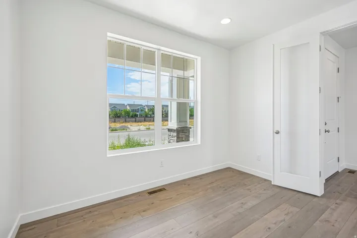 Bright interior space featuring a large window with white framing, wood-finish flooring, recessed ceiling lighting, and a white interior door with frosted glass panel
