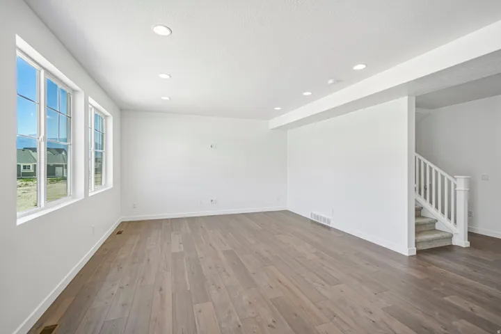 Spacious room featuring multiple large windows, recessed ceiling lighting, light wood-finish flooring, and a staircase with white balusters and carpeted treads