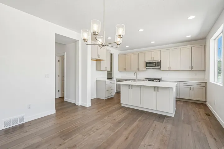 Modern kitchen featuring light gray cabinetry, a central island with integrated sink, stainless steel appliances, and light-toned countertops