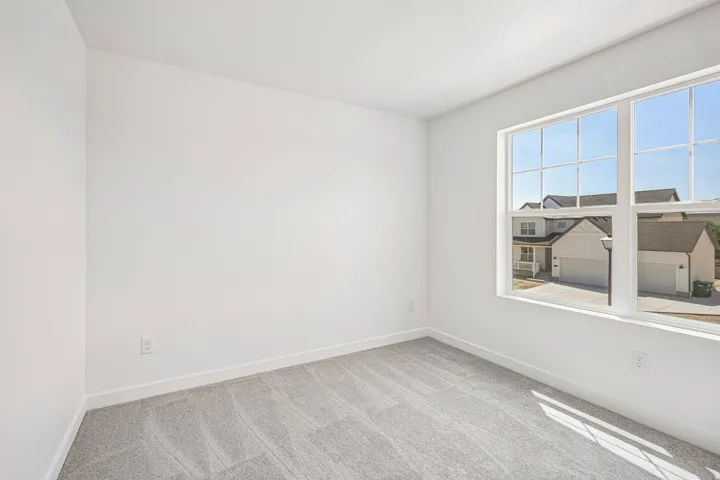 Bright interior space featuring a large multi-pane window, neutral-toned walls, and grey patterned carpeting