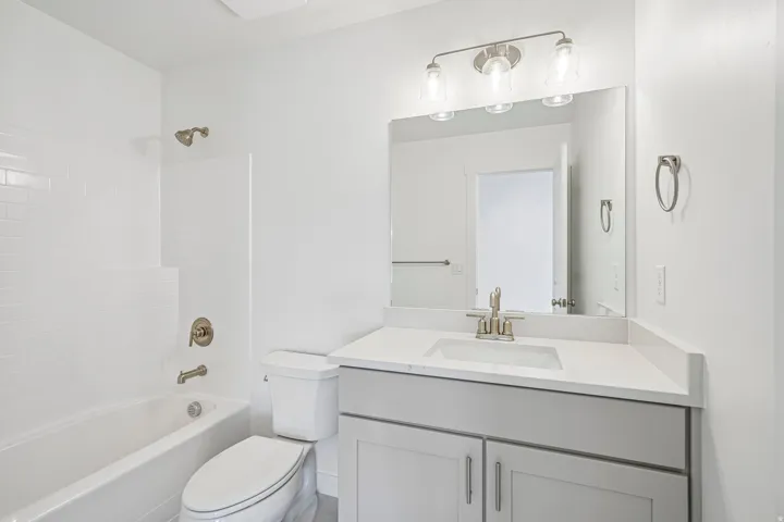 Bathroom featuring a white subway tile surround, brushed nickel fixtures, a single vanity with a white countertop, and a vanity mirror with a three-light fixture