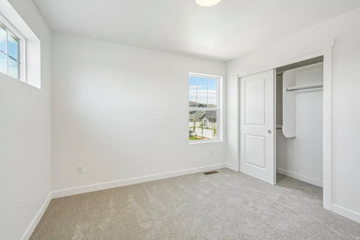 Carpeted interior space featuring white walls, a single window, an upper transom window, and a sliding two-panel closet