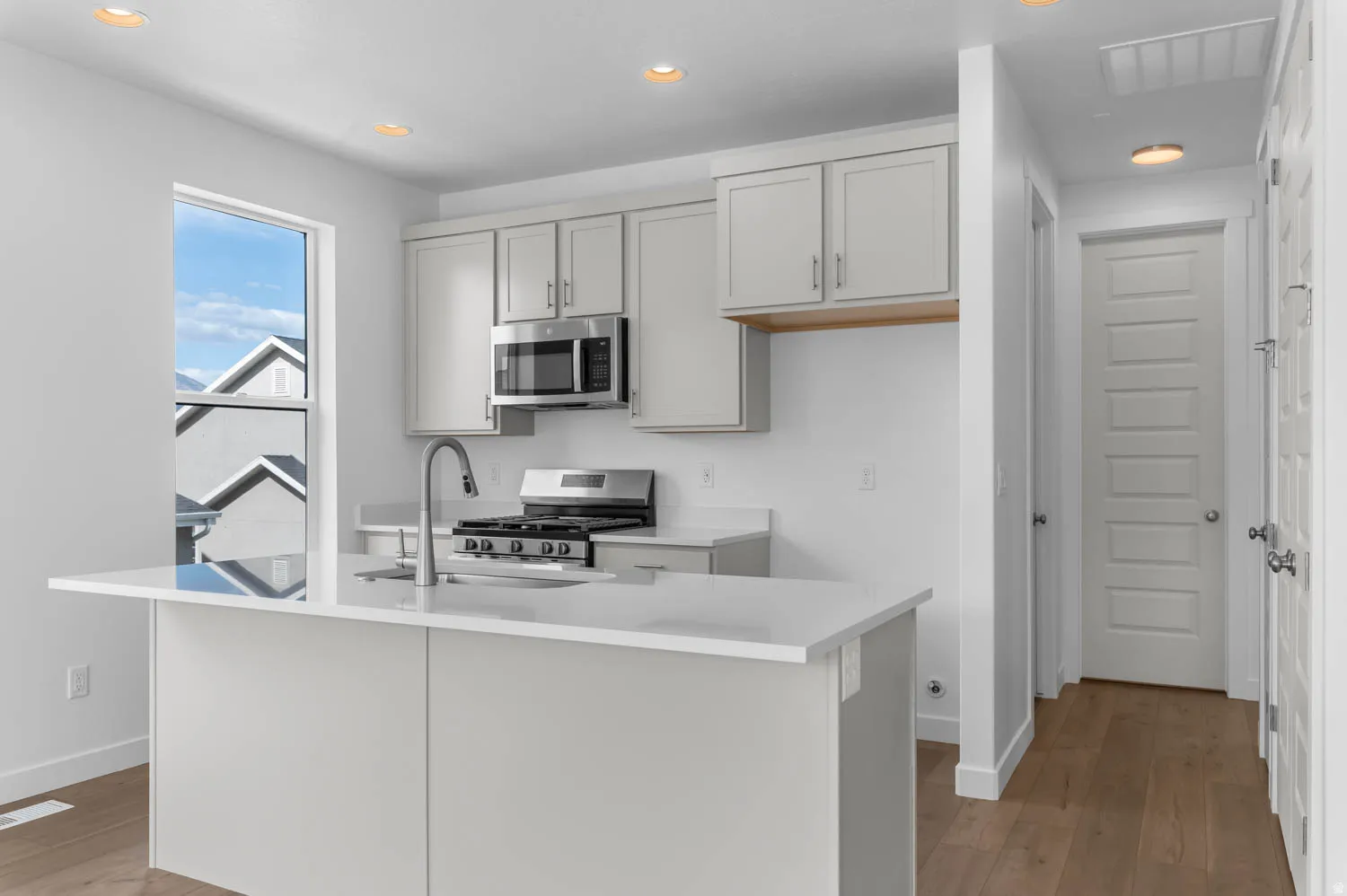 Modern kitchen featuring light gray cabinetry, stainless steel appliances, a center island with an integrated sink, and recessed lighting