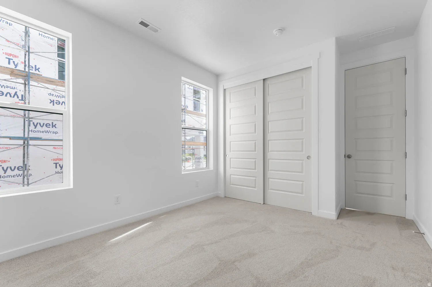 Bright room featuring two windows, light-toned carpeting, white walls, and a sliding panel closet door