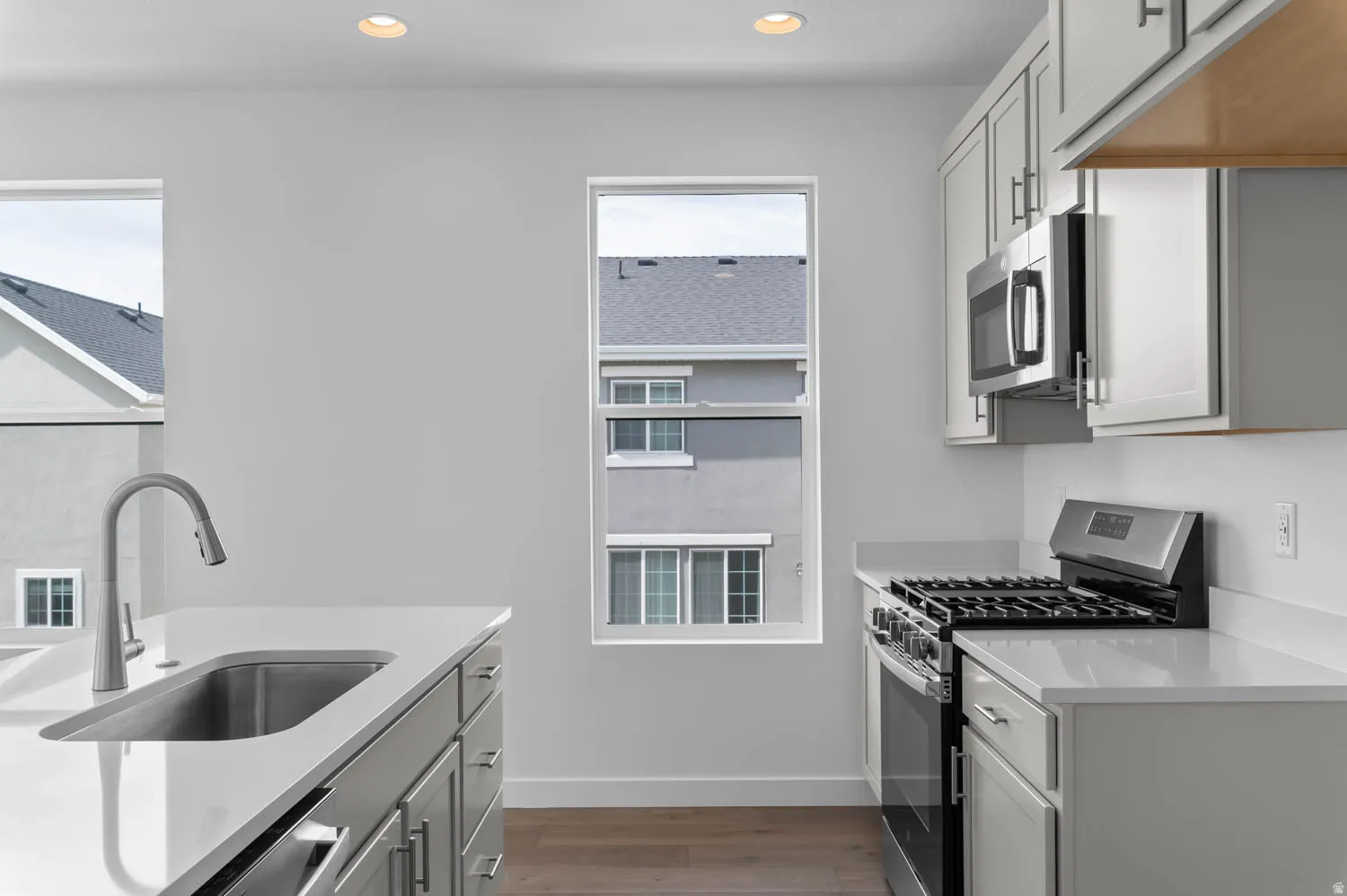 Modern kitchen featuring a stainless steel sink with a high-arc faucet, light-toned cabinetry with brushed nickel hardware, and a gas range with an overhead microwave