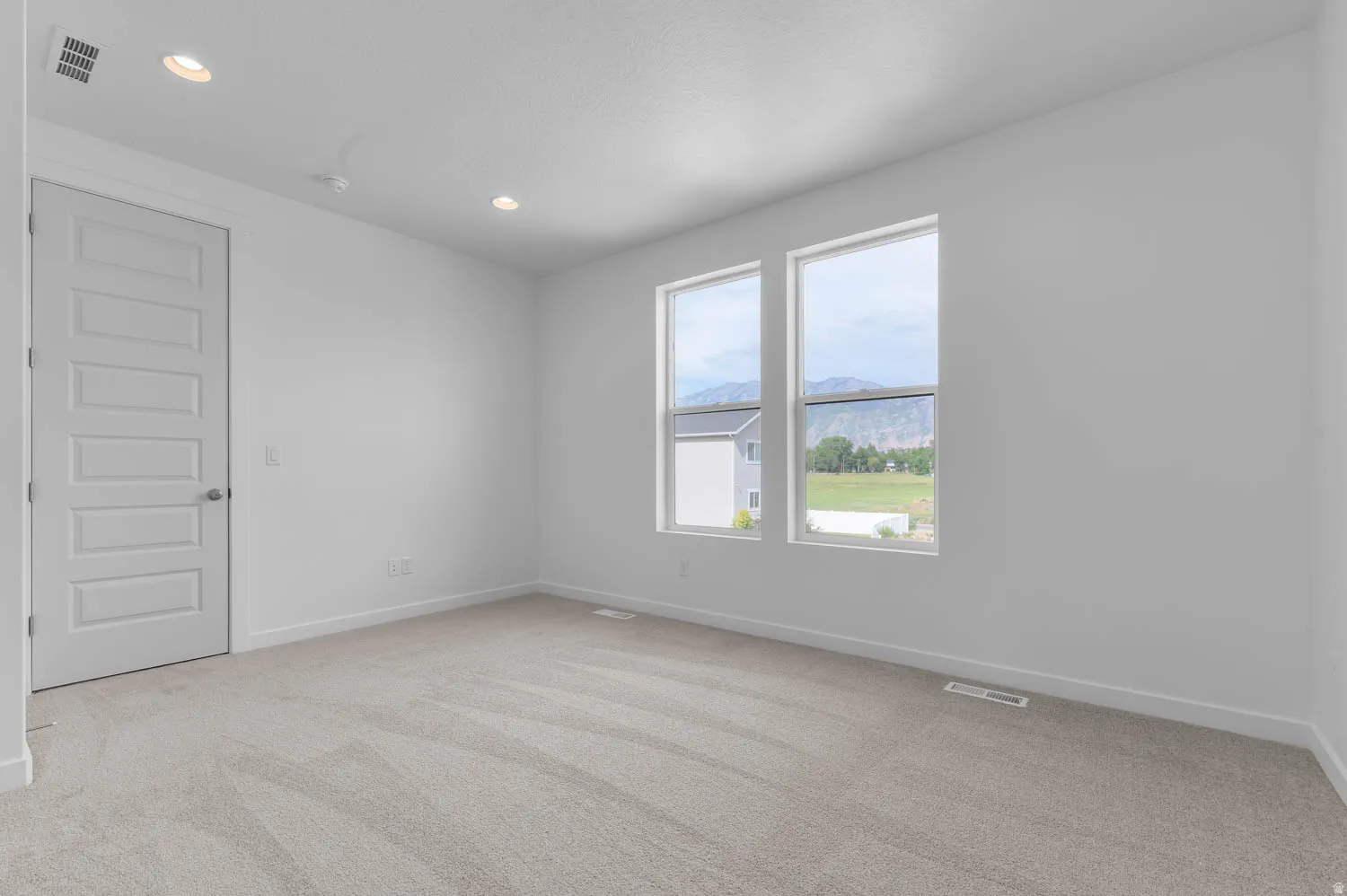Bright room featuring two large windows, recessed lighting, neutral-toned carpet, a five-panel interior door, and white baseboards