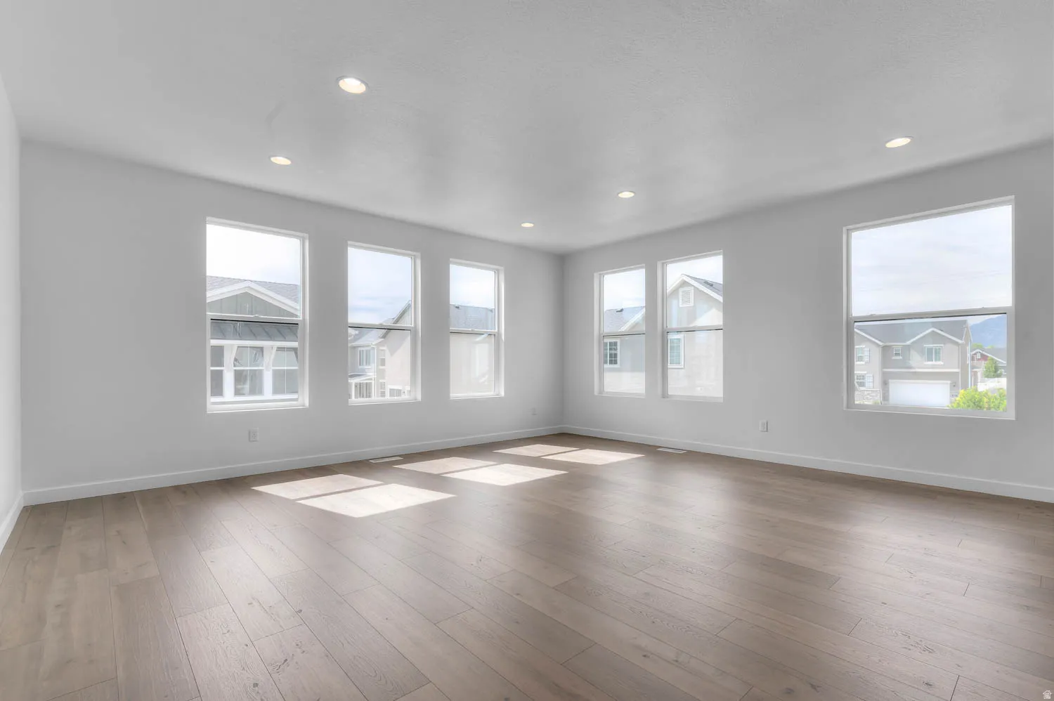 Spacious room featuring multiple windows, recessed lighting, white walls, white baseboards, and light wood-finish flooring