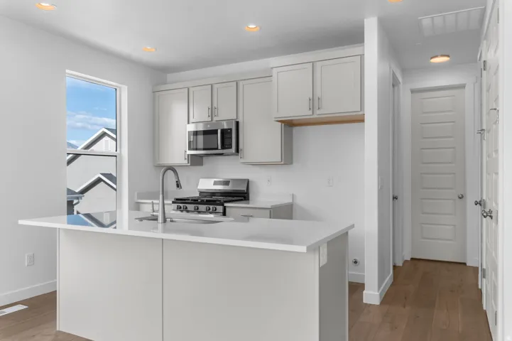 Modern kitchen featuring light gray cabinetry, stainless steel appliances, a center island with an integrated sink, and recessed lighting