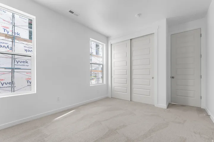 Bright room featuring two windows, light-toned carpeting, white walls, and a sliding panel closet door