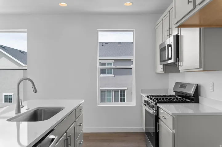 Modern kitchen featuring a stainless steel sink with a high-arc faucet, light-toned cabinetry with brushed nickel hardware, and a gas range with an overhead microwave