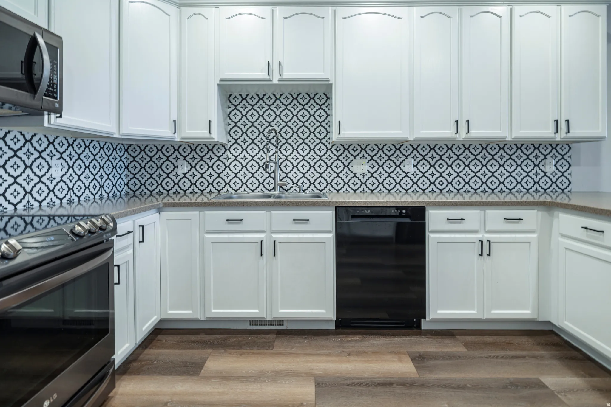 Kitchen featuring stainless steel appliances, white cabinetry, light stone counters, and dark wood-type flooring