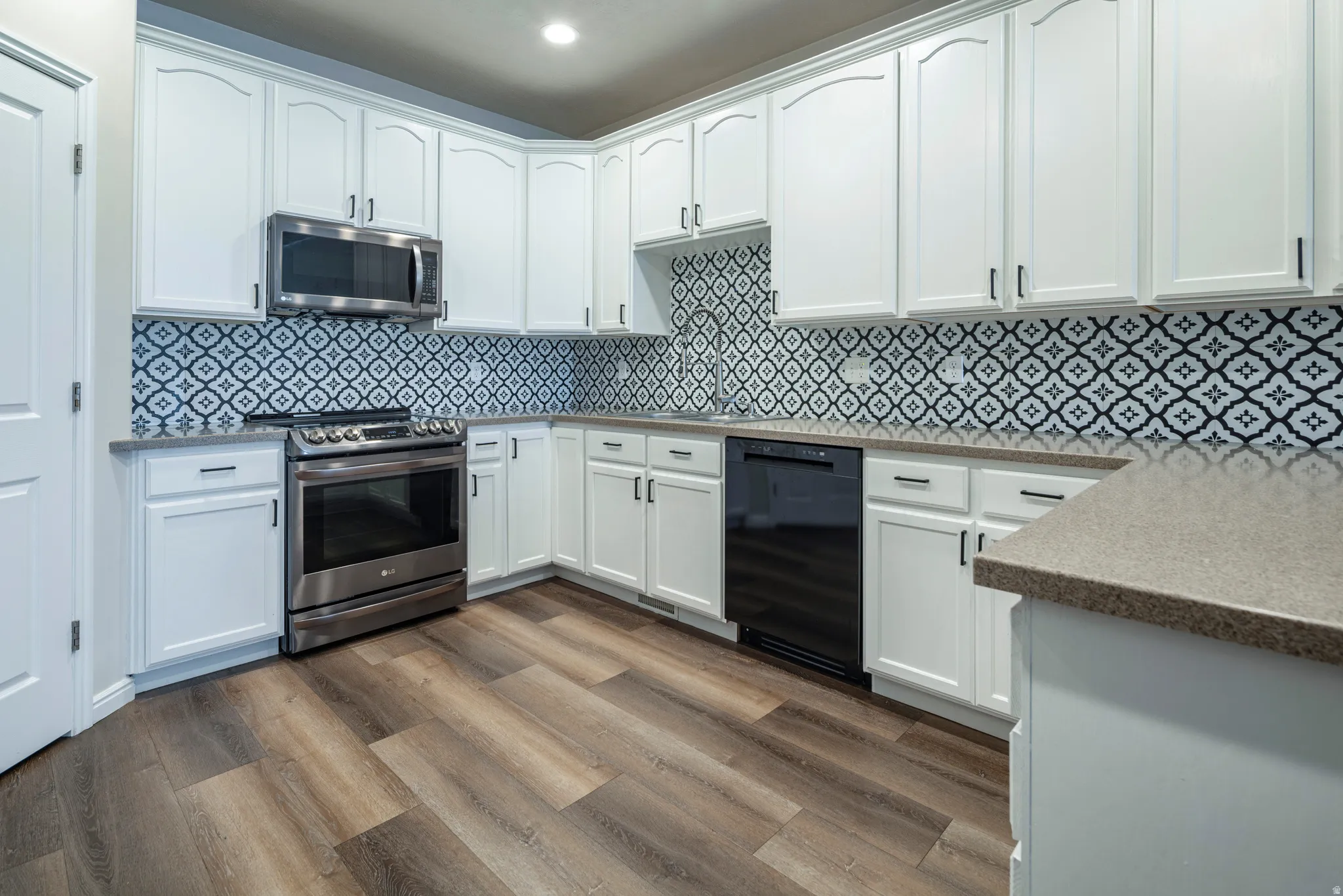 Kitchen featuring white cabinets, stainless steel appliances, dark wood-style floors, light stone countertops, and backsplash