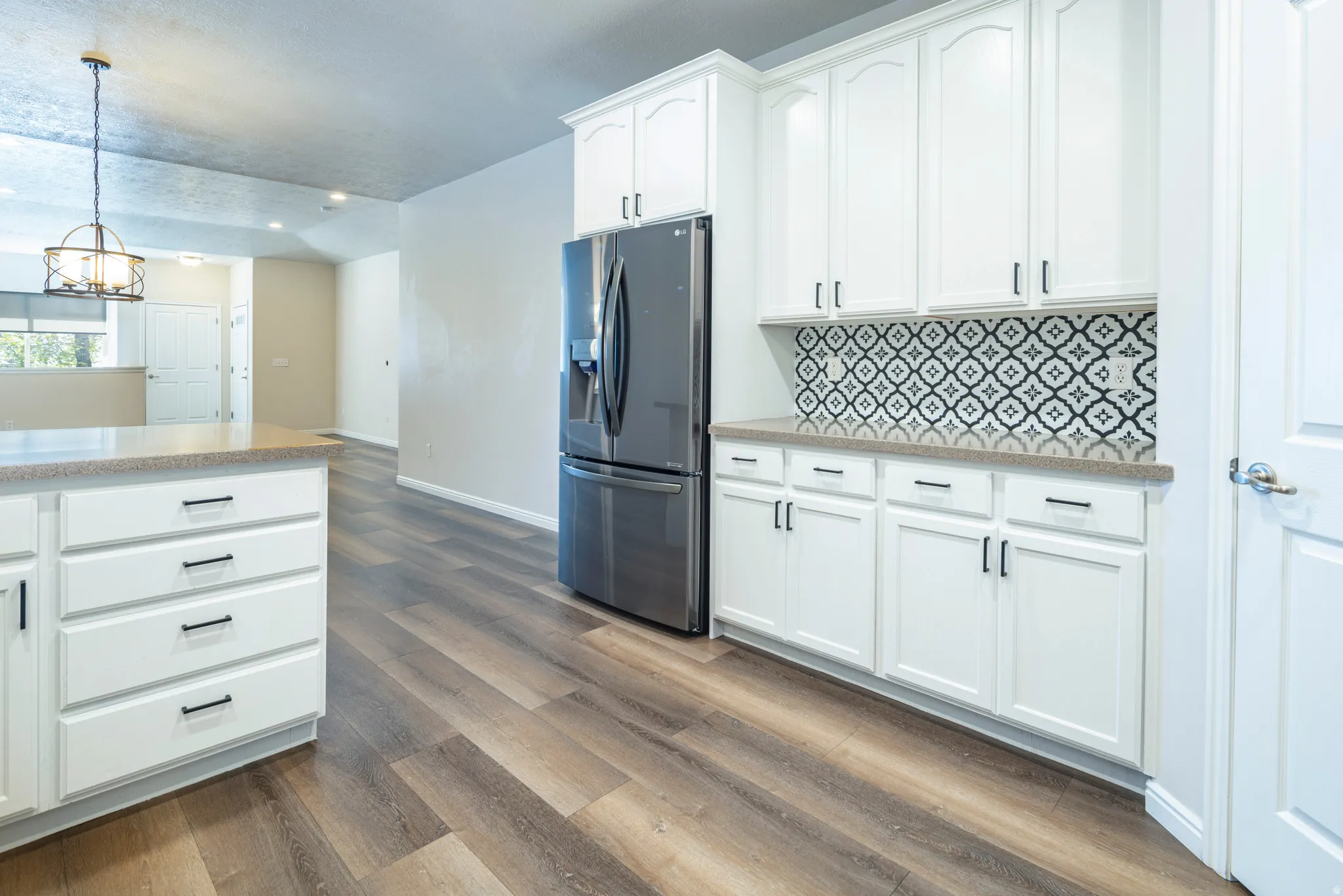 Kitchen featuring stainless steel refrigerator with ice dispenser, white cabinetry, dark wood-style flooring, a chandelier, and light stone counters