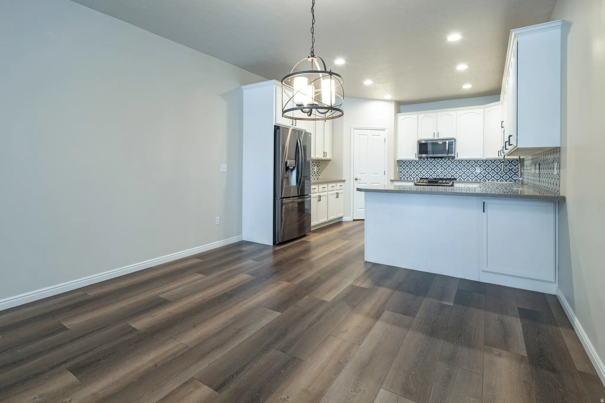 Kitchen with white cabinets, a peninsula, stainless steel appliances, dark wood-style floors, and tasteful backsplash